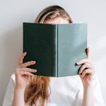 Unrecognizable student behind book studying in sunlight