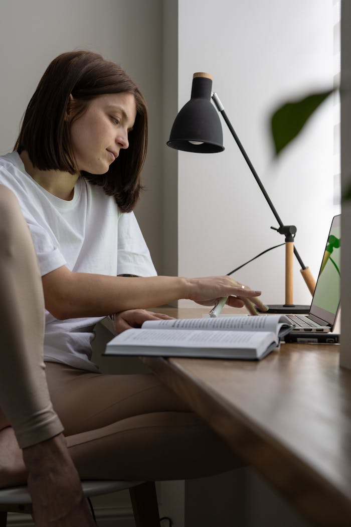 Young female freelancer working online on laptop and reading book